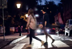Two people crossing at night and a car is speeding towards them.