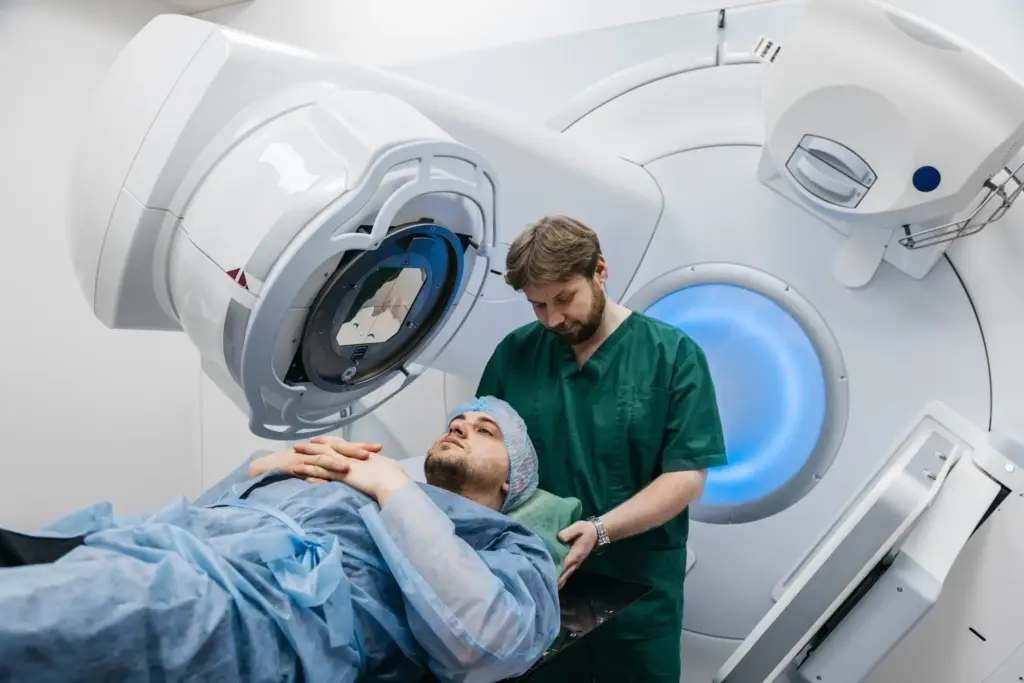 A man about to do radiation therapy and a nurse is helping set up.