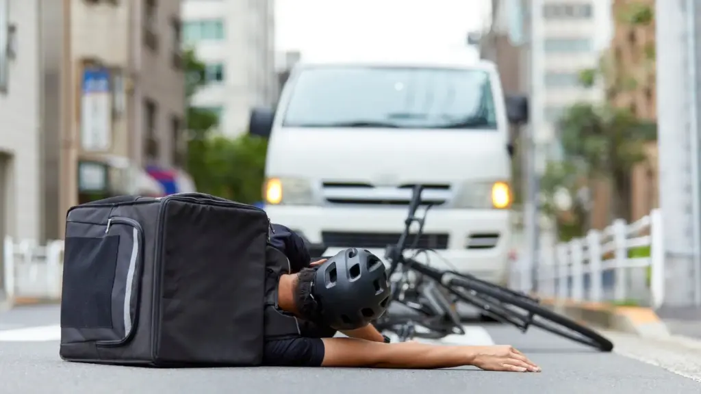 A biker laying in the middle of the road with an oncoming car.