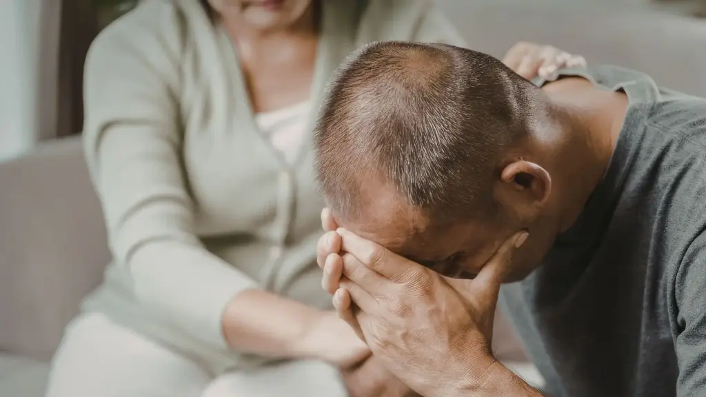 A grieving man getting comforted by a woman.