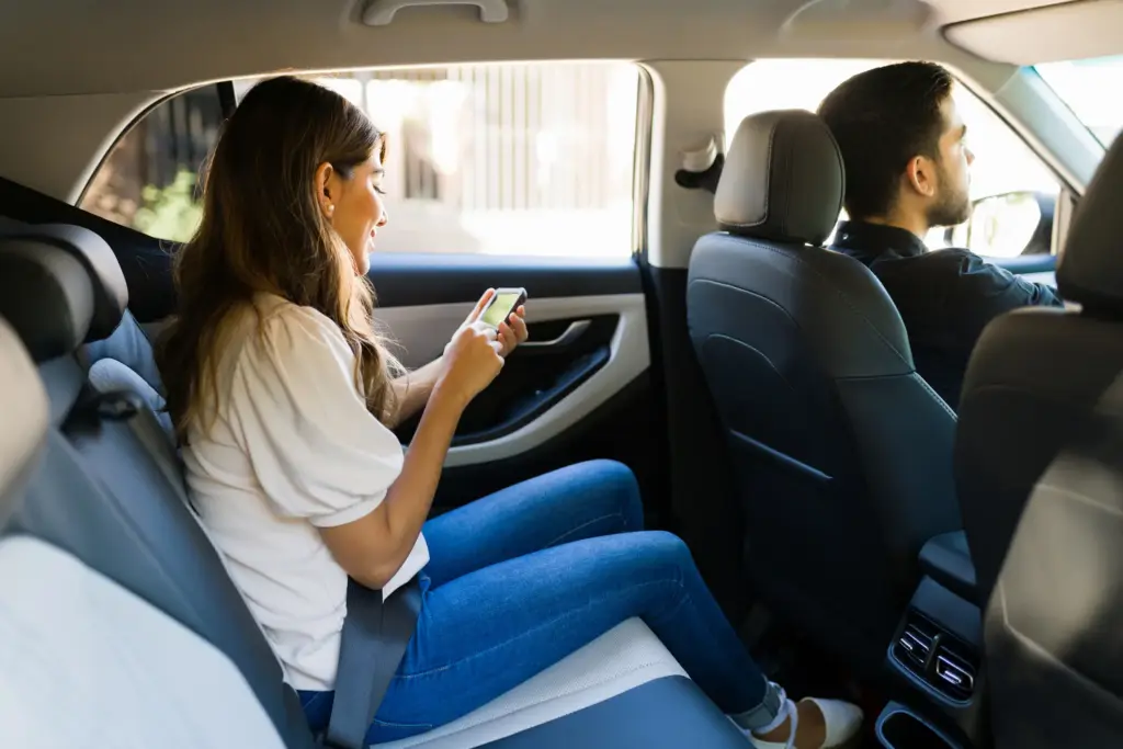 A woman riding in a rideshare service while on her phone.