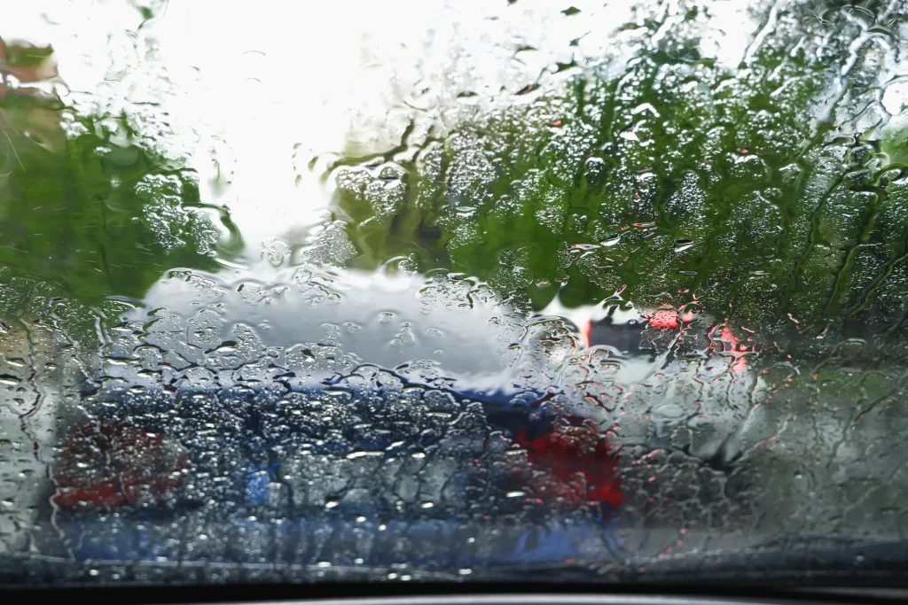 A rainy day from the perspective of a driver looking at two cars through a wet windshield.