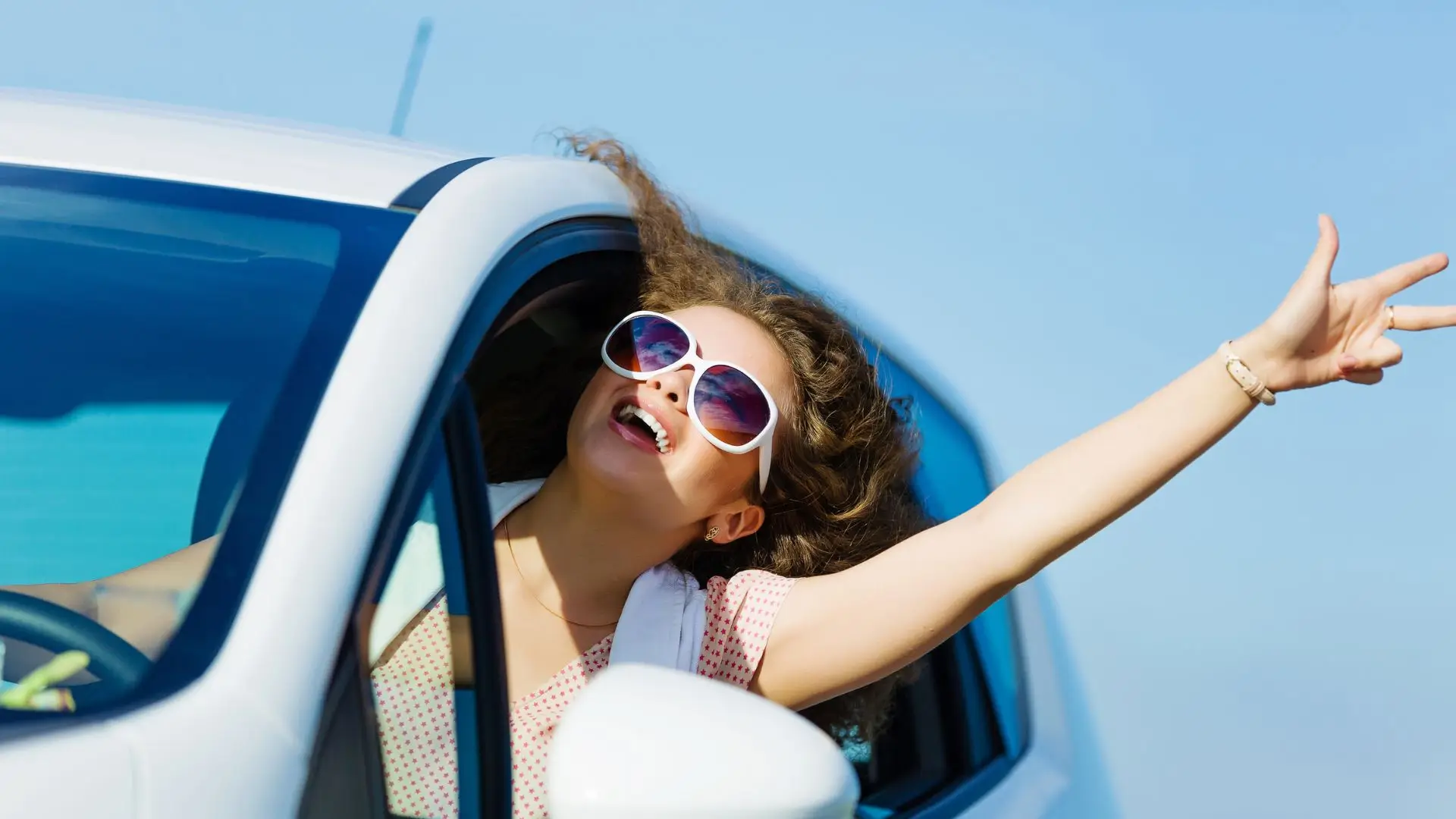 A woman sticking her head and arm out while driving.