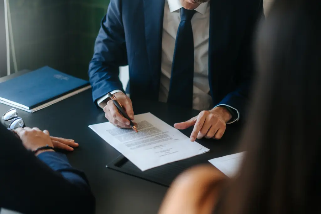 An attorney signing a document with two people standing in front of him.