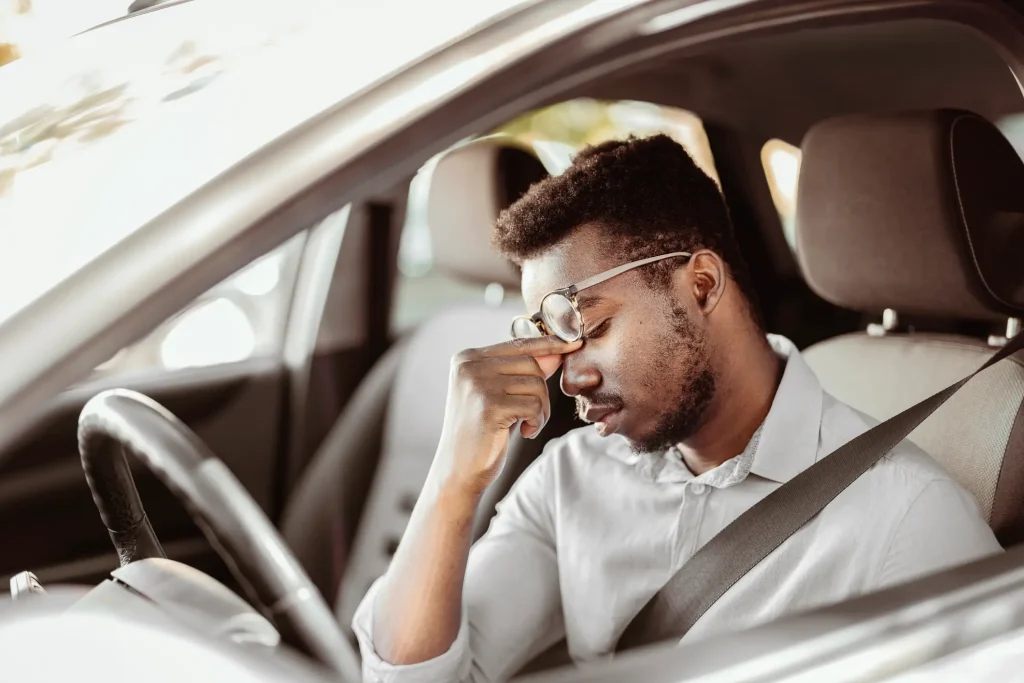 A man pinching his nose in his car, indicating his fatigue.