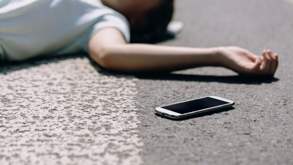 A woman laying on the street with her phone right next to her.