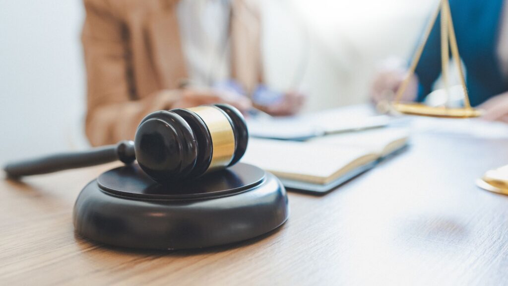 Gavel on a wooden desk with attorney and client in the background.
