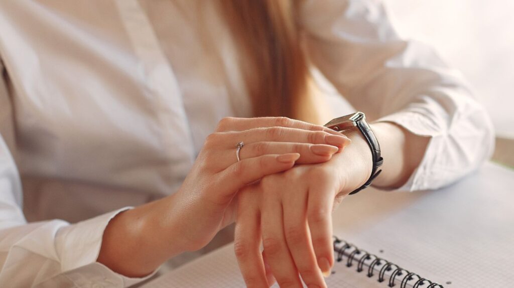 Woman sitting at a desk with her notebook open and looking down at her watch.