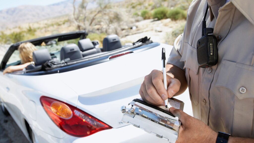 Highway officer writing a fix-it ticket for a driver.
