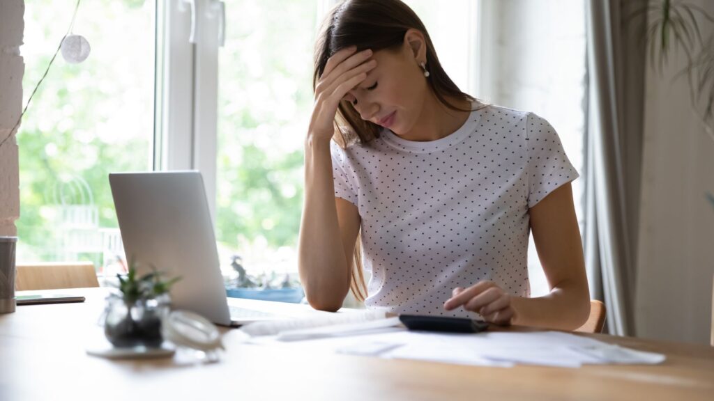 A woman with paperwork and laptop in front of her looking sorrowful.
