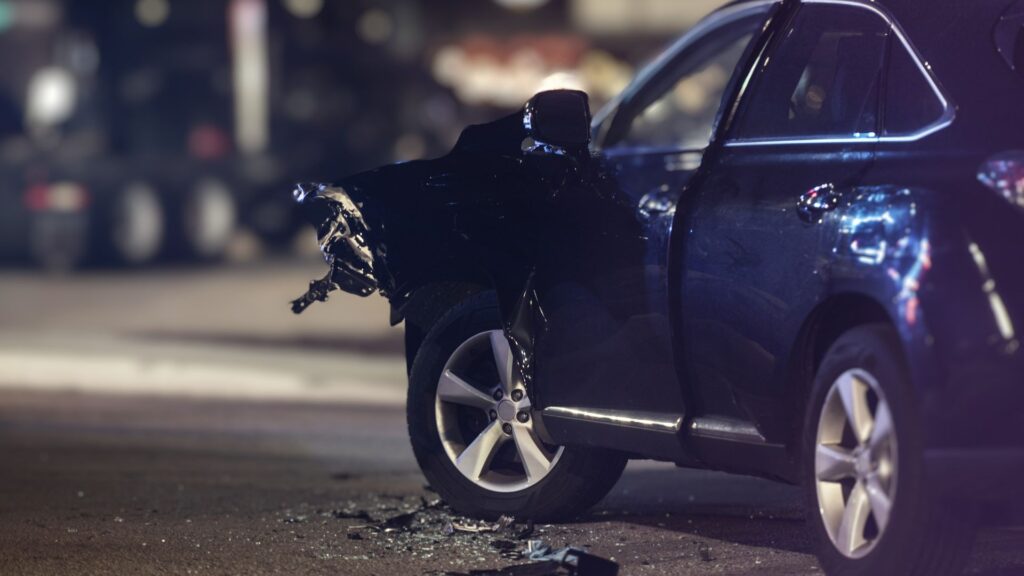 A damaged blue car on a street at night.