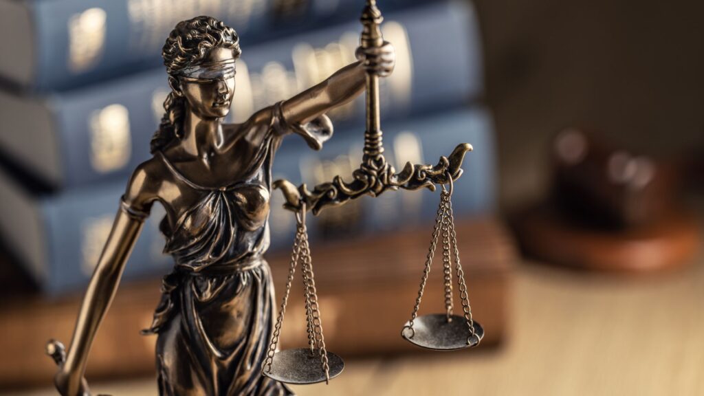 A statue of lady justice in front of a stack of books.