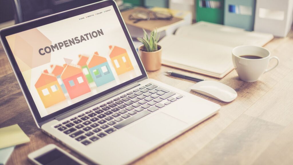 Una laptop encima de un escritorio de madera con la palabra "compensación" en la pantalla.