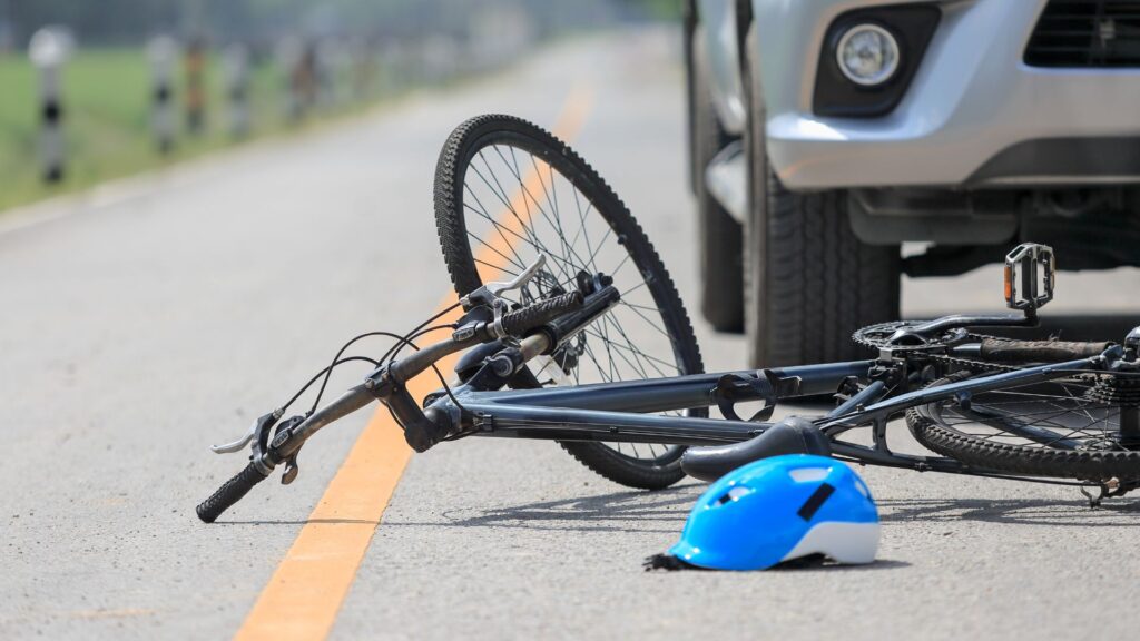 A bike and helmet on the road with a car in front.