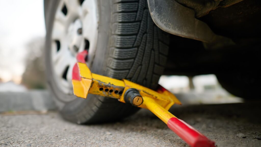 A yellow wheel clamp locked onto a car's tire.