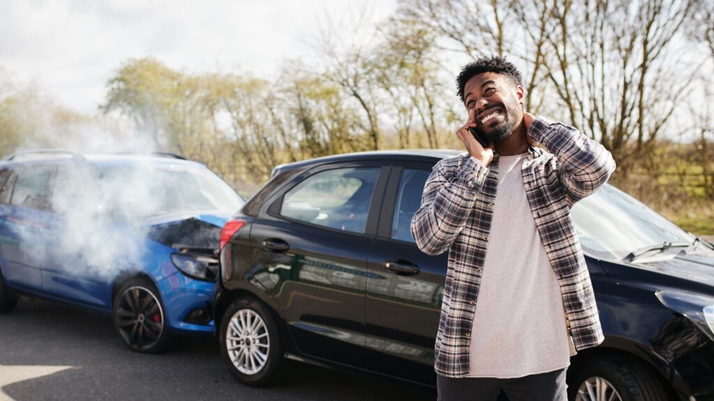 A man on the phone in front of two crashed cars.