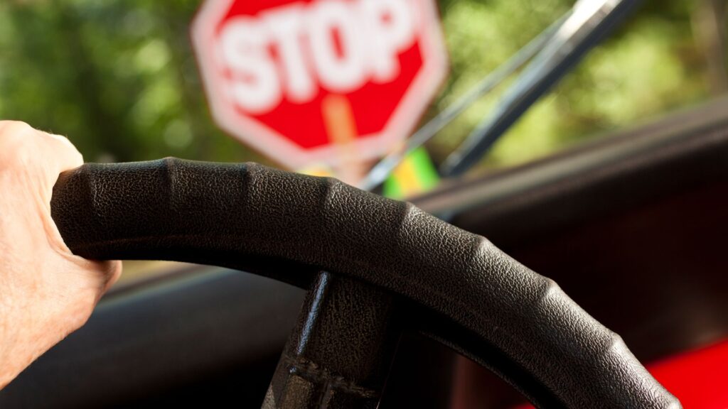 A person with a hand on the steering wheel is pulling up to a stop sign.