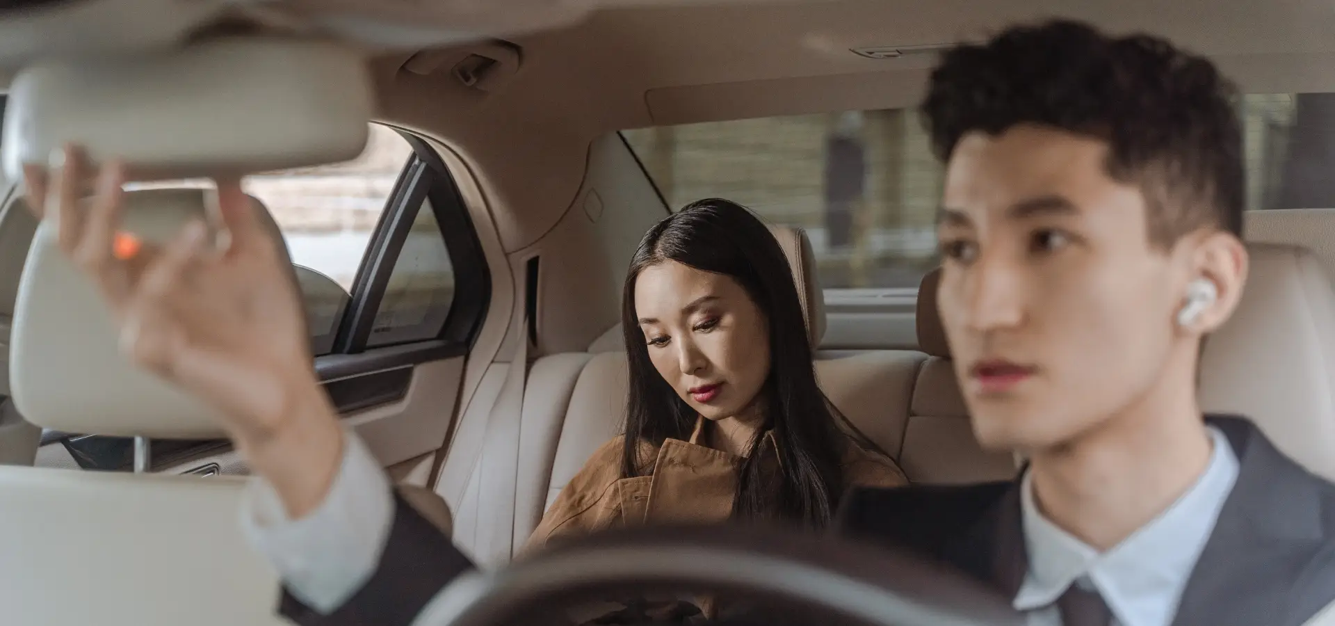 A Uber Driver adjusting his mirror while his passenger is looking down at her phone.