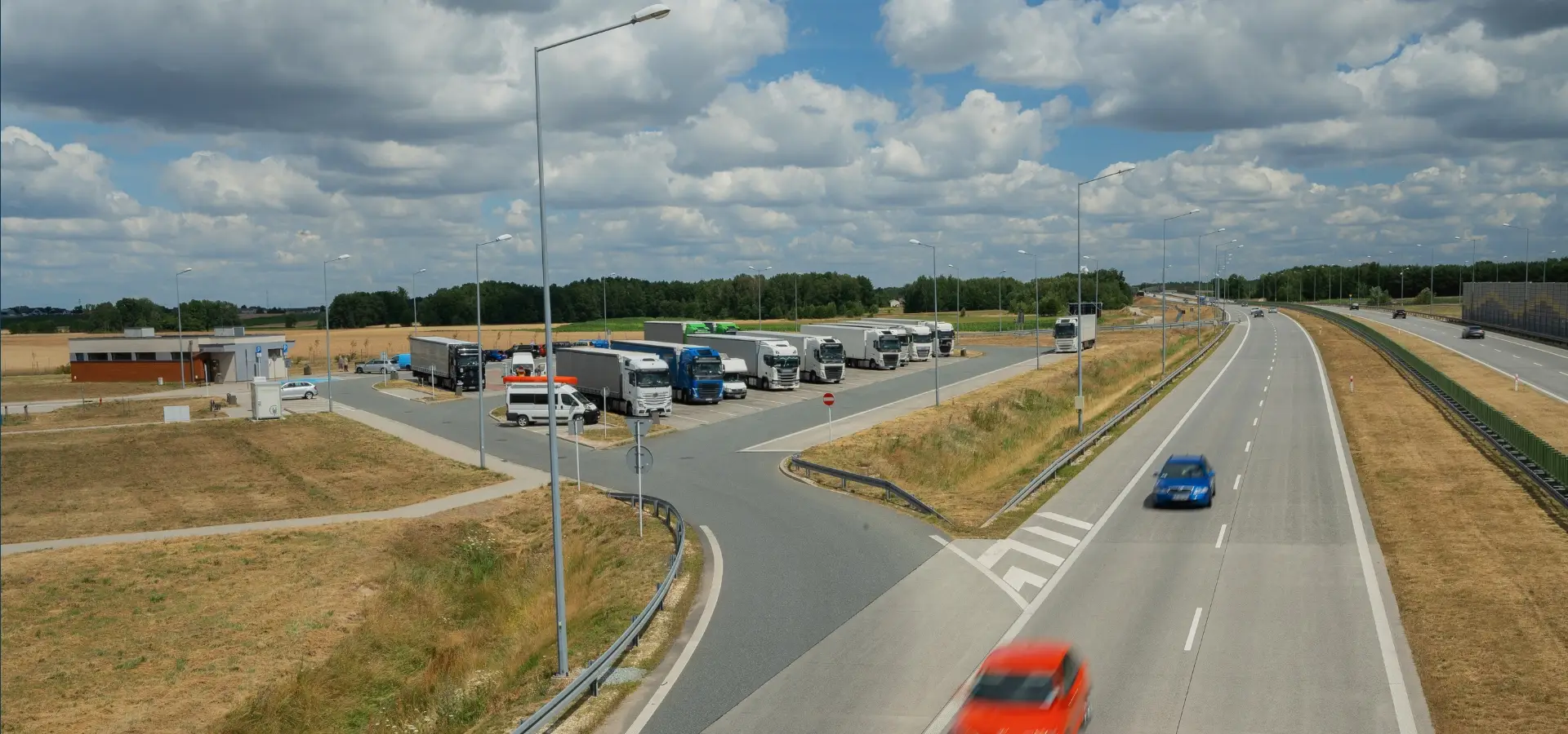 A rest stop with a lot of trucks and cars by an freeway.