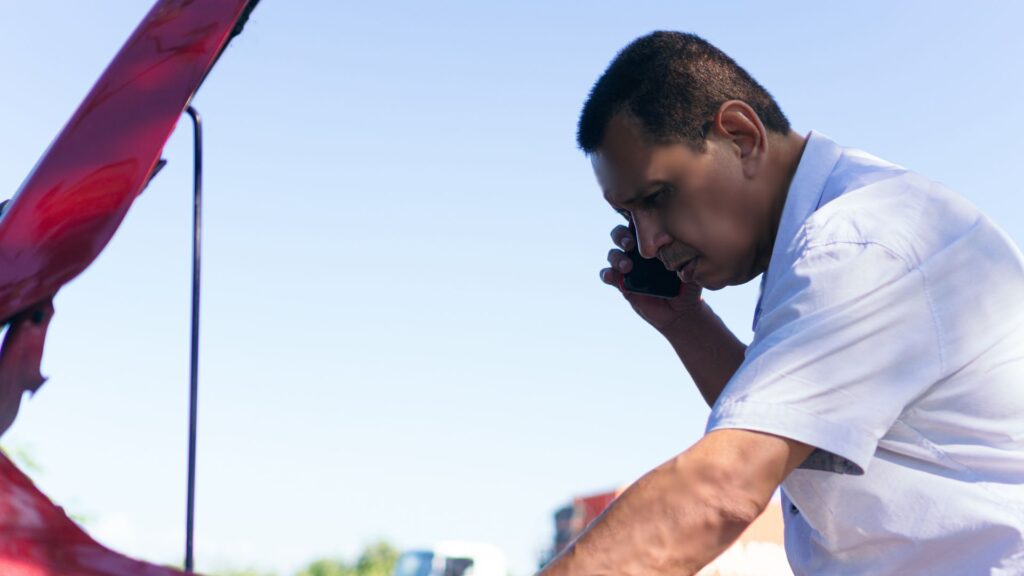 Hombre chequeando el daño a su carro mientras llama por ayuda.