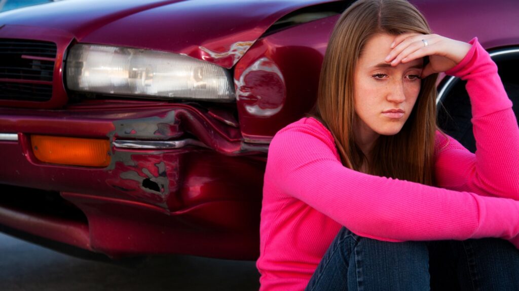 A woman sitting in front of her car after getting into a car accident.