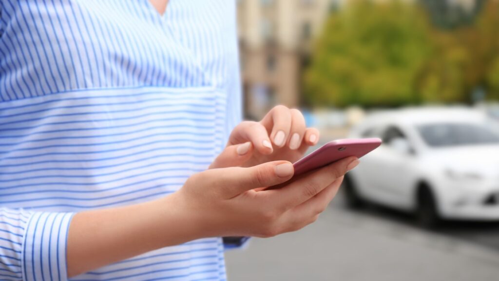 Una mujer usando su teléfono celular para llamar un servicio de viaje compartido.