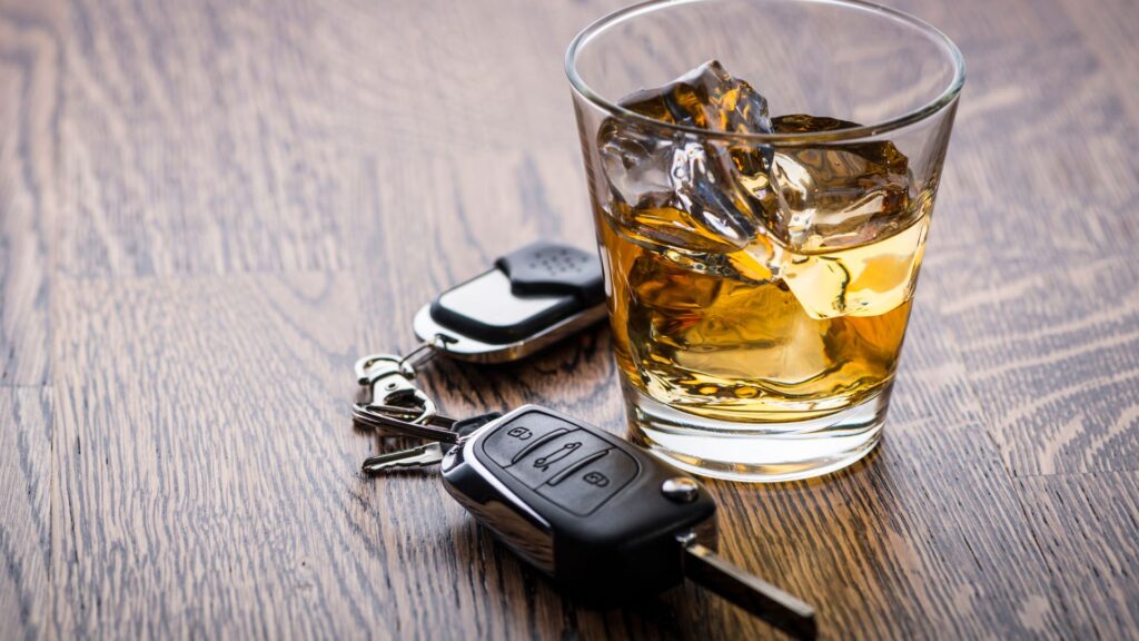 A glass of whiskey and a set of car keys on a table.