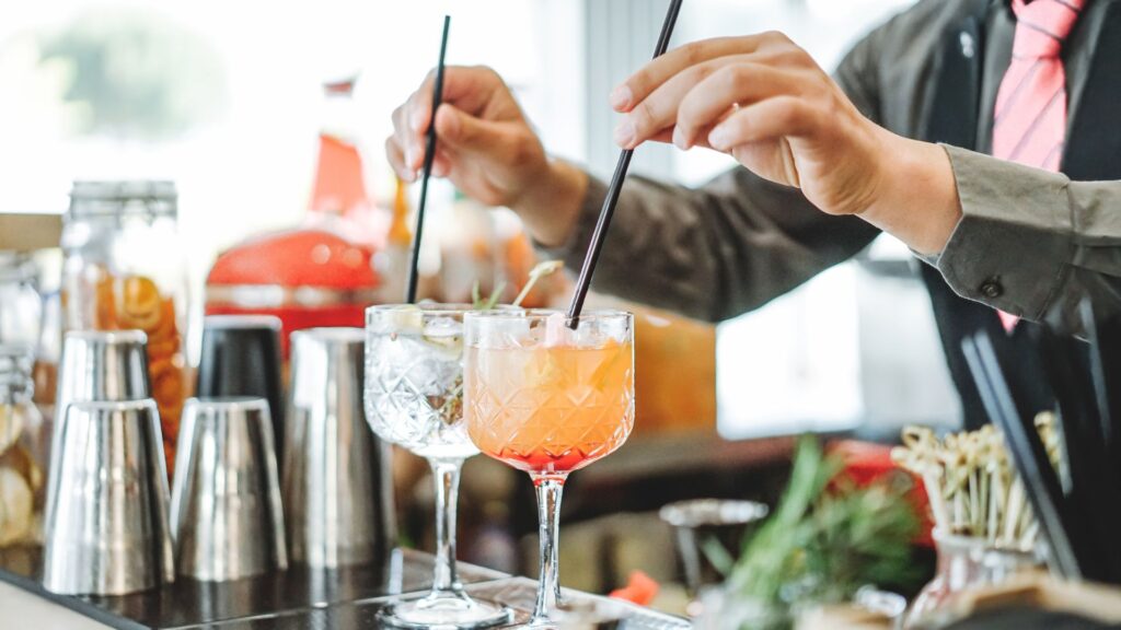 A bartender making two fruity cocktails.