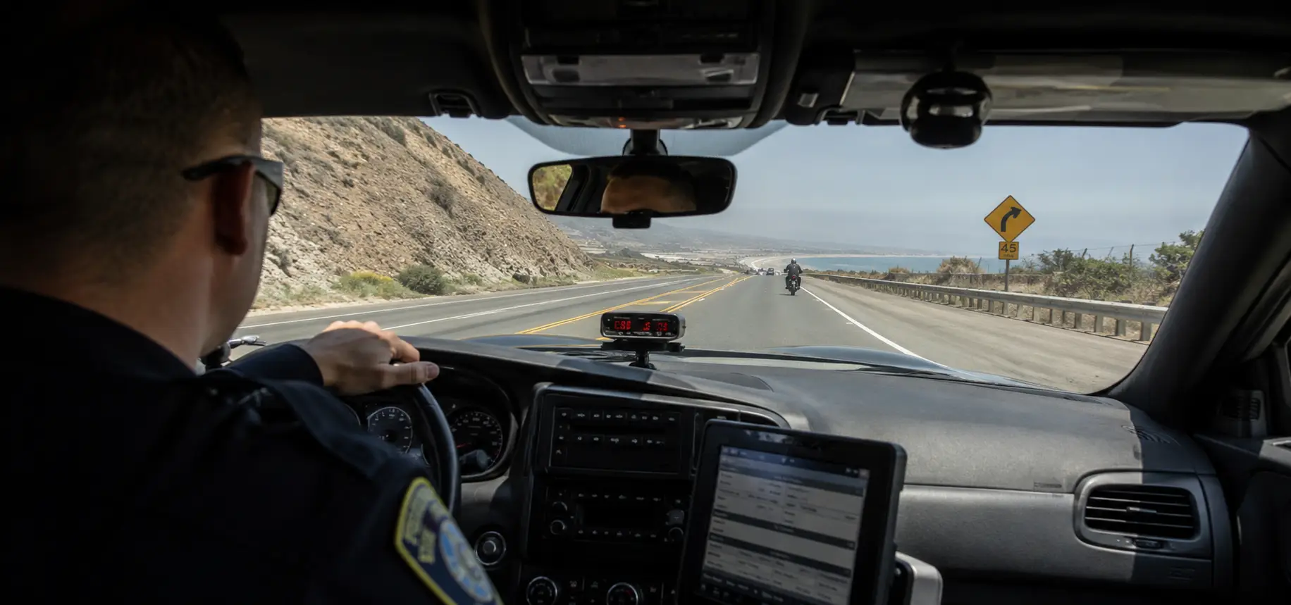 A police officer chasing after a motorcyclist in his car.