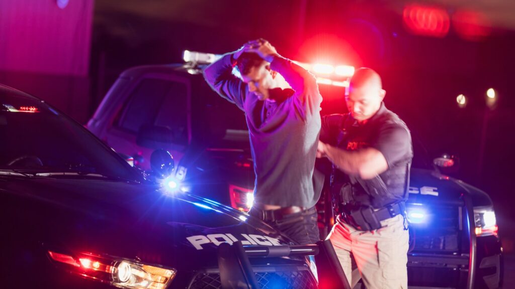 A man amid two lit up police cars at night being arrested for a DUI.