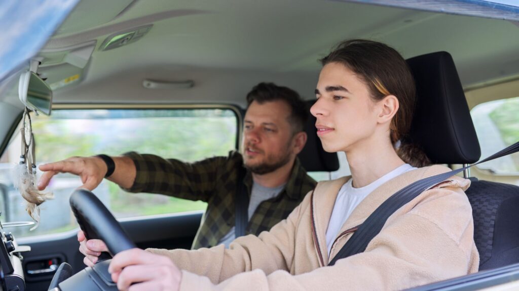 A teenager driving a car and their father is teaching them from the passenger seat.