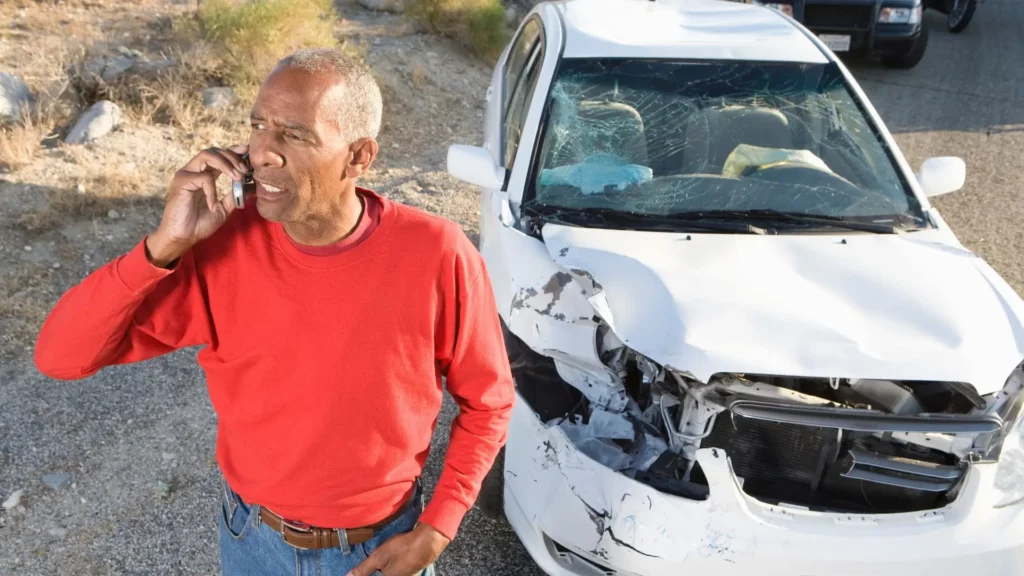 An old man on the phone after getting involved in a car accident in the desert.