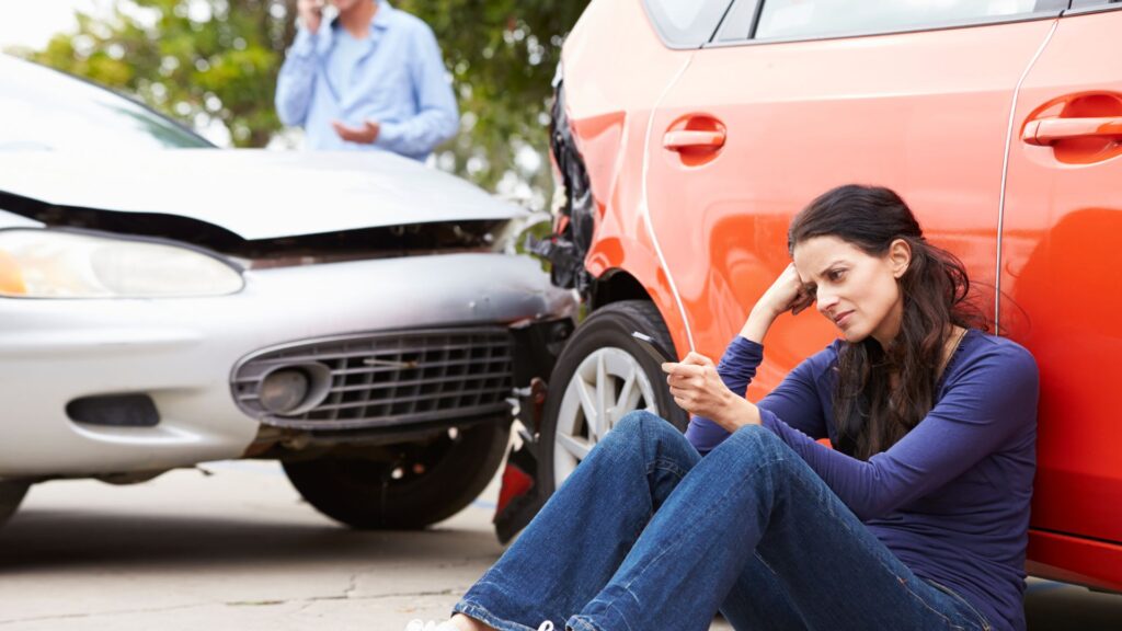 A woman sitting by her wrecked car after getting into a car accident.