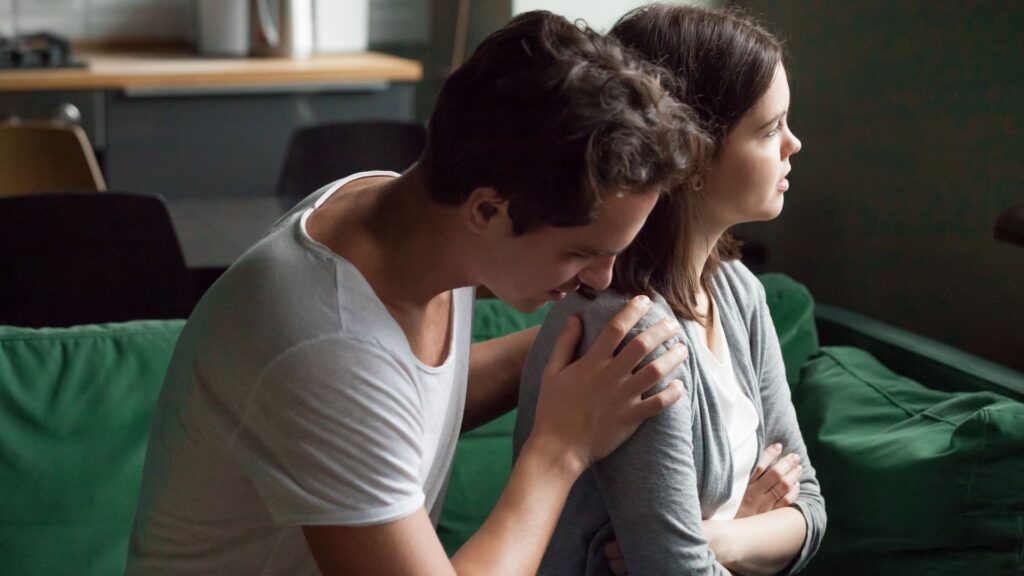 A man consoling a woman as she looks out to the distance.