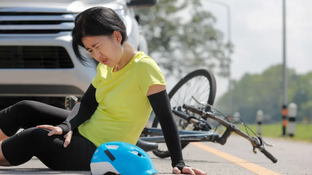 A female biker sitting on the road after getting hit by a car.