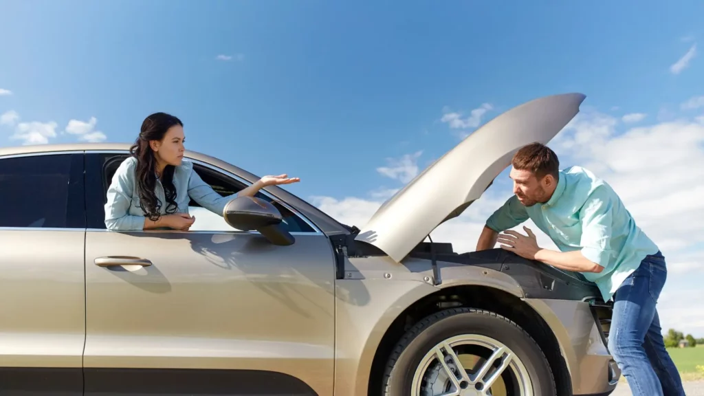 A man trying to fix a tan car and a woman telling him something.
