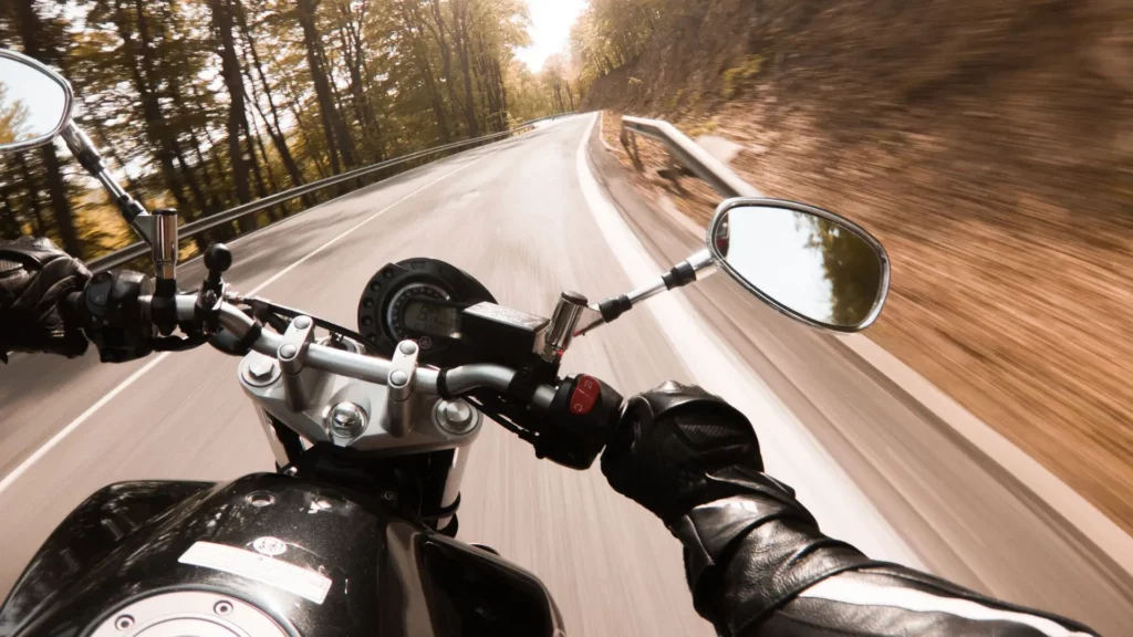 A POV shot of a motorcycle rider, driving on a narrow road surrounded by trees.