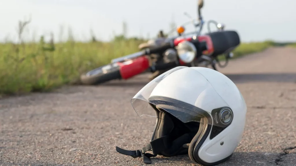A white helmet and red motorcycle lying on the side of the road.