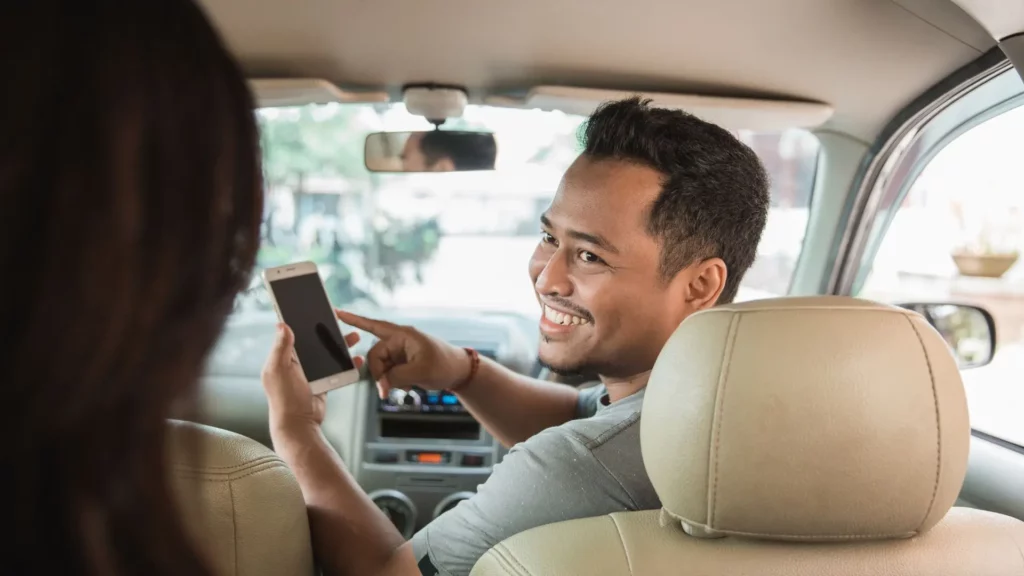 A car passenger showing his phone to the passenger in the back.
