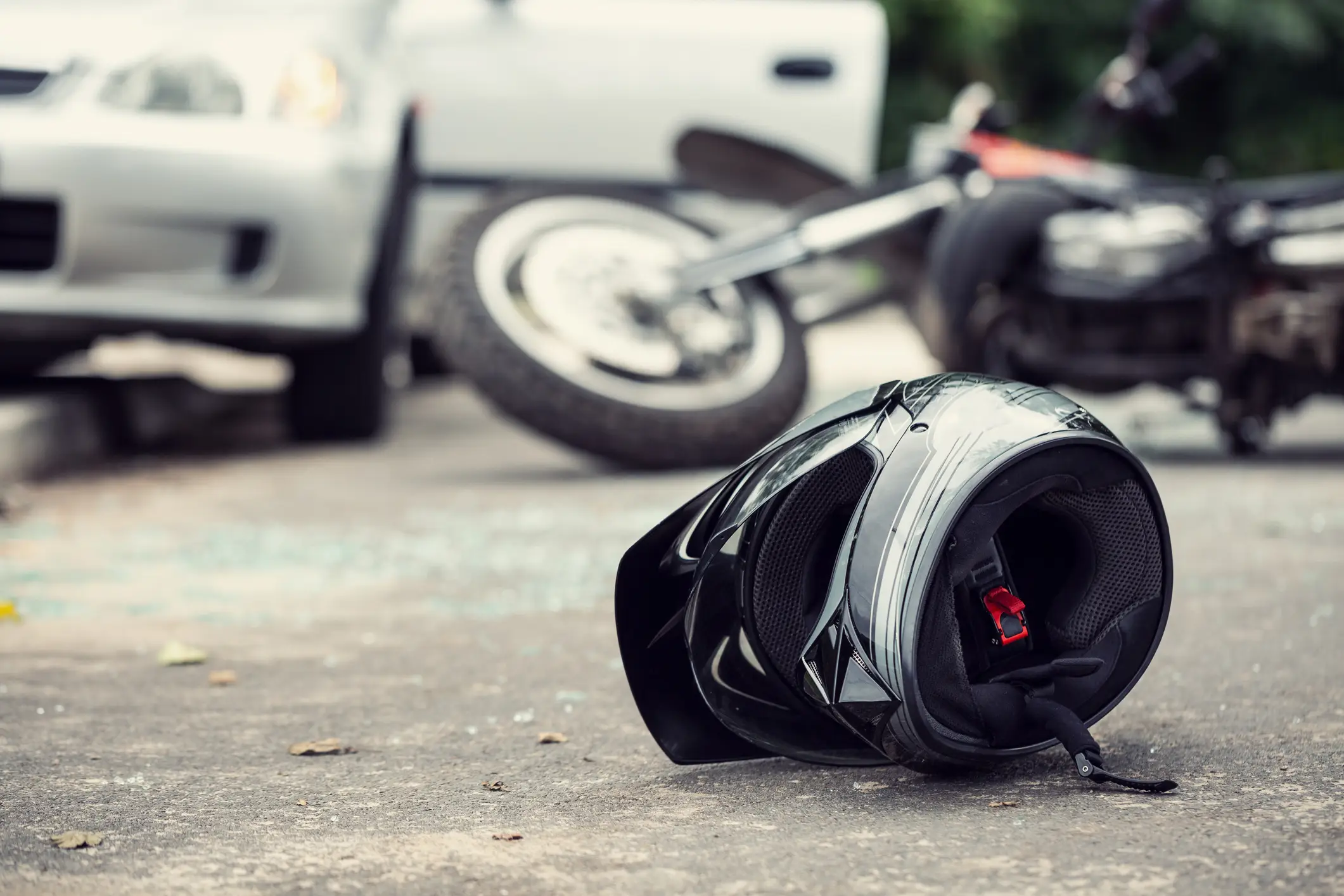 A motorcycle accident where a helmet and bike are on the ground after hitting a car.