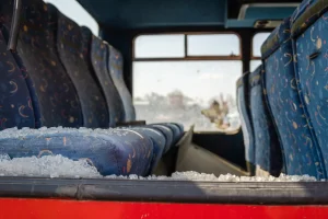 A bus with a broken window, showing broken glass all over the seats.