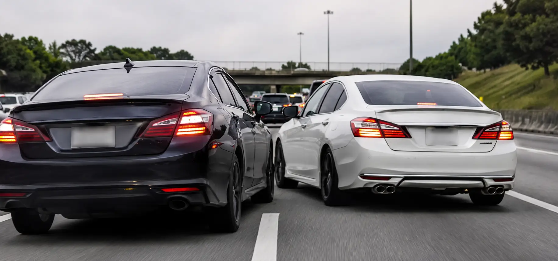 Two cars side-by-side on a multi-lane highway, both angled slightly toward the same lane, with brake lights on and a tense but non-crash moment.
