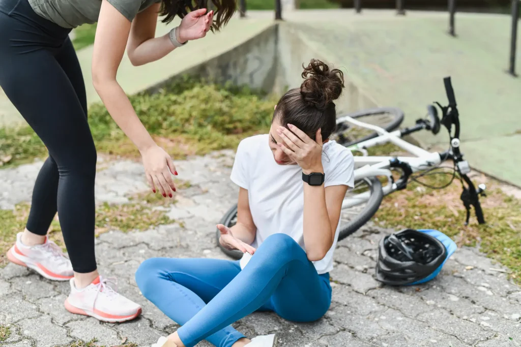 A woman on the ground holding her head in pain after a bike accident.