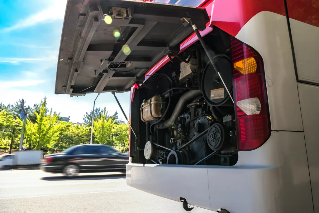 A bus stopped in the road, with the engine hood propped open.