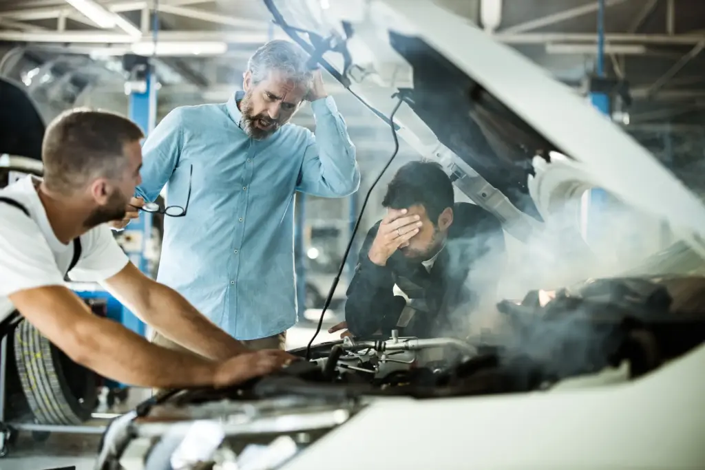 A car smoking when a mechanic is looking at it and the owner is stressed.