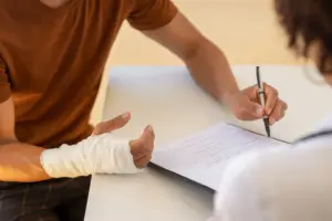 A man with a broken arm signing some paperwork.