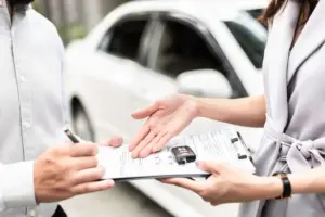 A person signing a document with a pair of car keys on top.