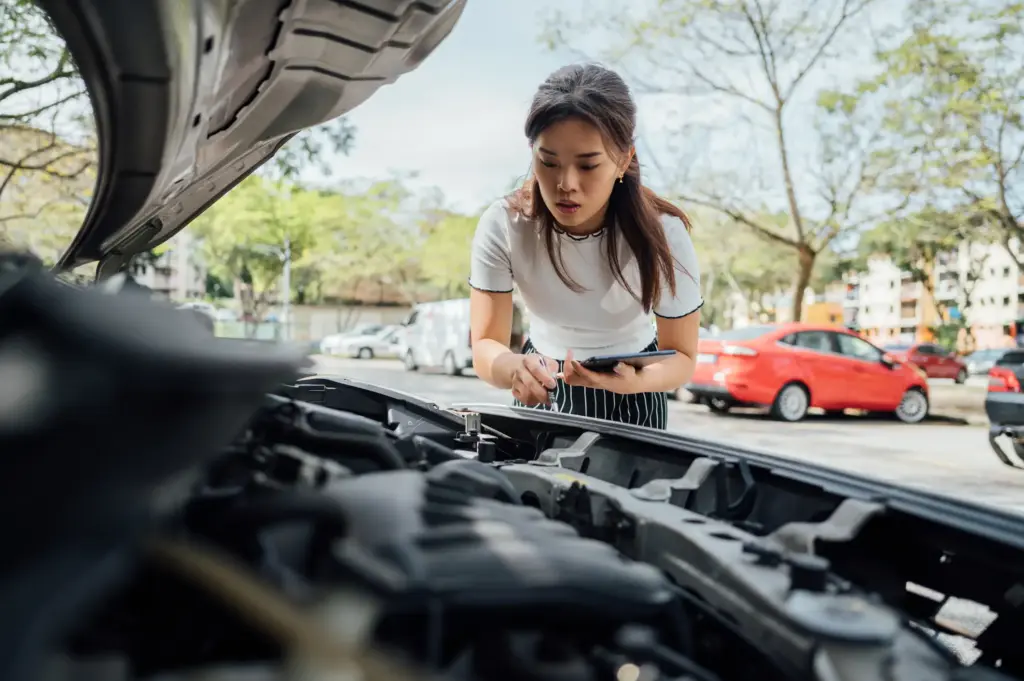 Una mujer preocupada mirando el motor de su auto.