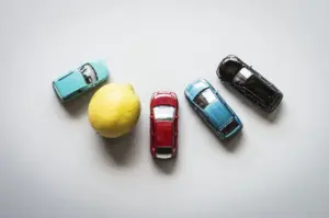 A row of 4 toy cars and a lemon placed in the middle.