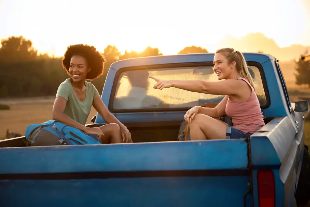 Two girls riding in the back of a pickup truck.